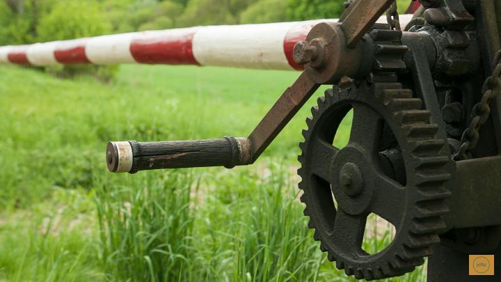 Rusty mechanical arm with gear and lever, in a grassy field.